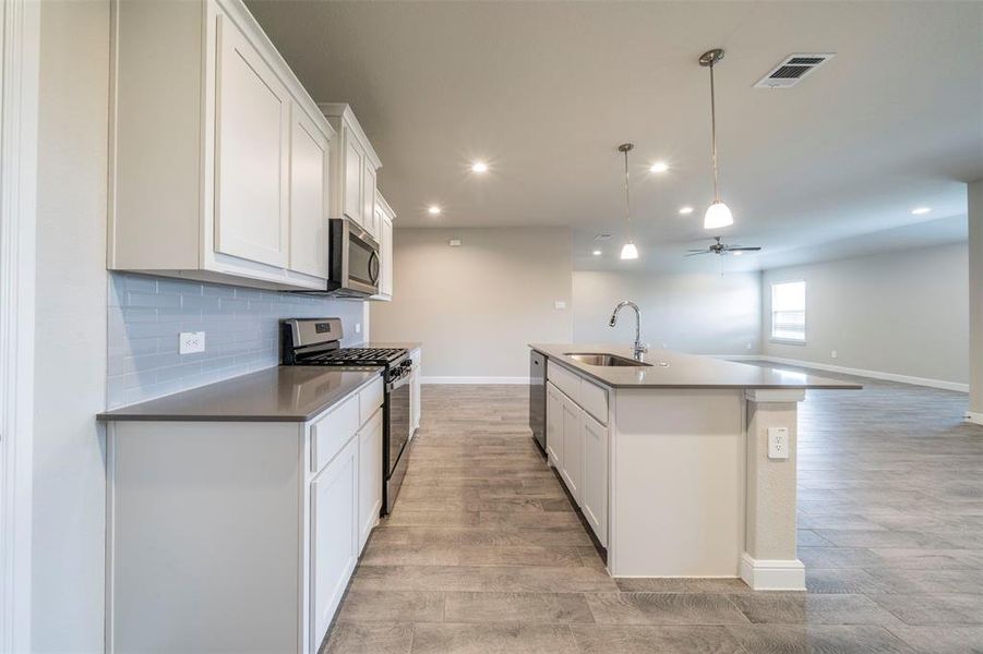 Kitchen with appliances with stainless steel finishes, light hardwood / wood-style floors, white cabinetry, sink, and a kitchen island with sink