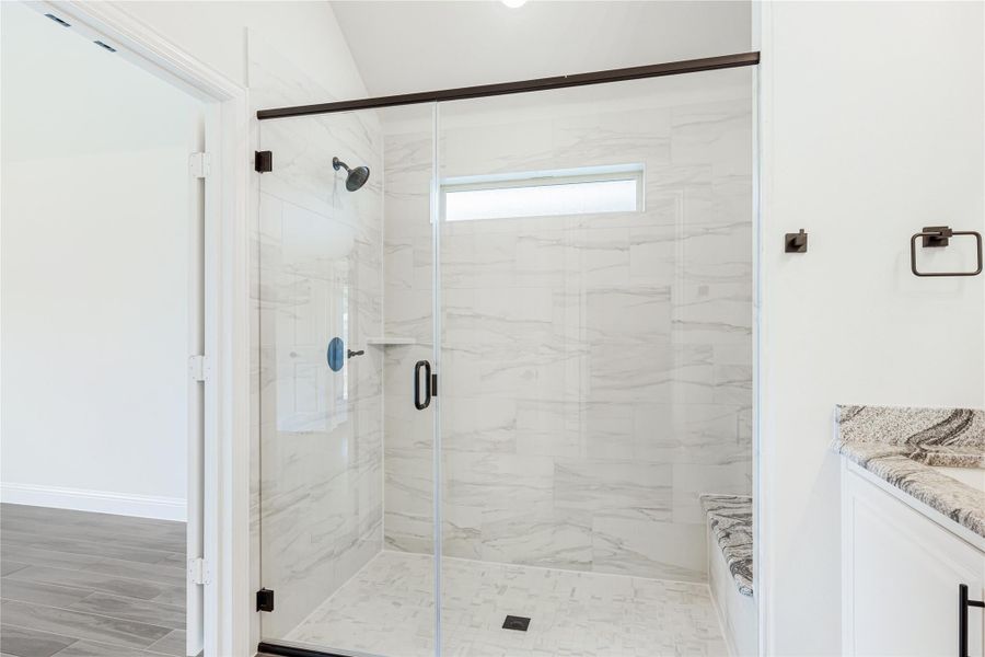 Walk-in shower with marble tile walls, glass door, dark hardware, and a small window above Walk-in shower with marble tile walls, glass door, dark hardware, and a small window above