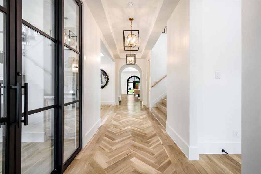 Entryway featuring iron-framed glass double doors, herringbone wood-finish flooring, a coffered ceiling, and three geometric pendant lights Entryway featuring iron-framed glass double doors, herringbone wood-finish flooring, a coffered ceiling, and three geometric pendant lights