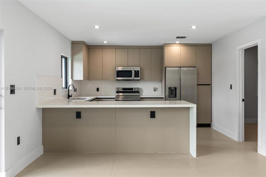 Kitchen featuring flat-panel cabinetry, quartz countertops with a waterfall edge, stainless steel appliances, recessed lighting, and large-format tile flooring