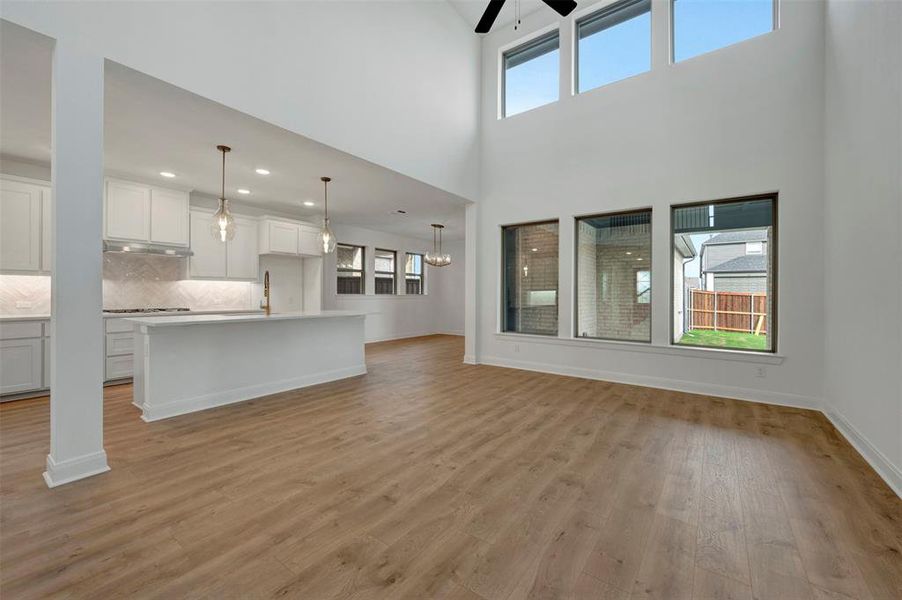 Unfurnished living room with light wood finished floors, ceiling fan, a high ceiling, and suspended lighting