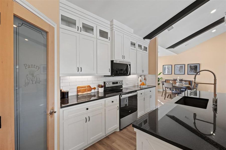 Kitchen featuring white shaker cabinetry with dark hardware, dark countertops, a white subway tile backsplash, and stainless steel appliances Kitchen featuring white shaker cabinetry with dark hardware, dark countertops, a white subway tile backsplash, and stainless steel appliances