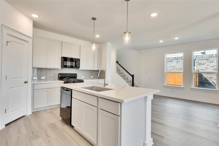 Kitchen with decorative backsplash, white cabinetry, a center island with sink, black appliances, and pendant lighting Kitchen with decorative backsplash, white cabinetry, a center island with sink, black appliances, and pendant lighting