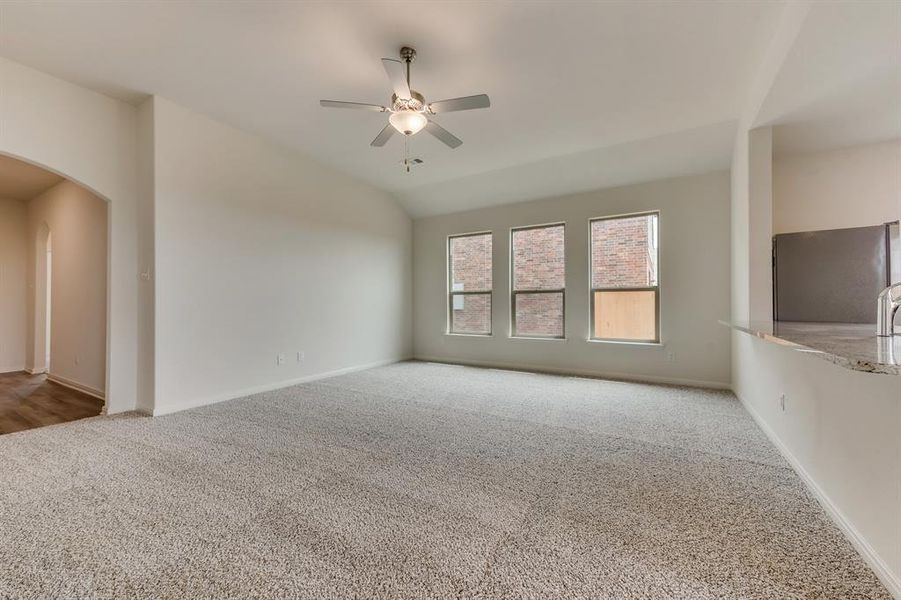 Unfurnished living room featuring carpet flooring, vaulted ceiling, and ceiling fan