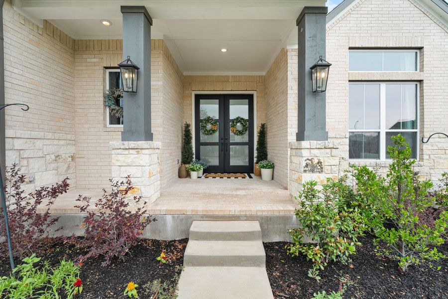 A welcoming stone and brick facade features prominent double doors flanked by tasteful landscaping and inviting outdoor lighting.