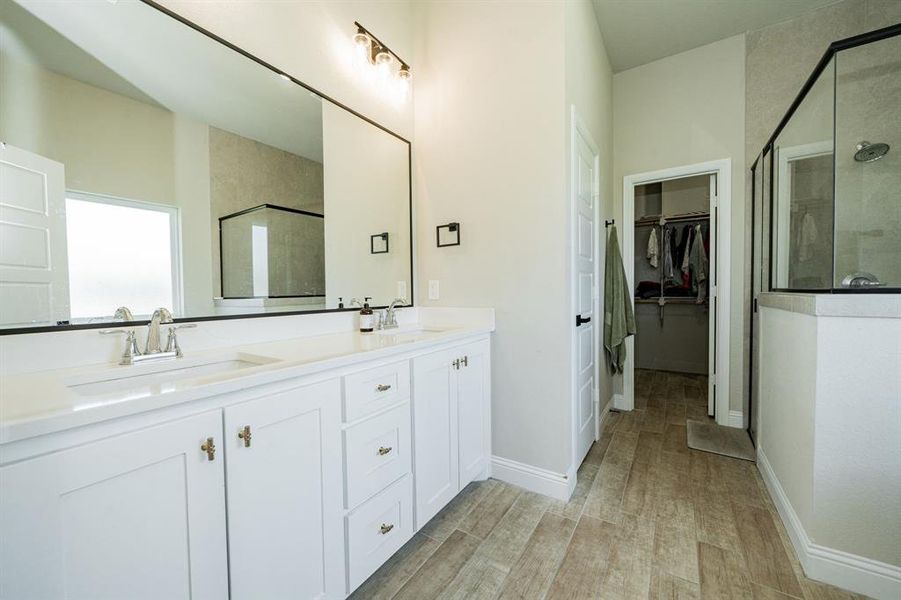 Full bathroom featuring a shower stall, a walk in closet, double vanity, and light wood finished floors Full bathroom featuring a shower stall, a walk in closet, double vanity, and light wood finished floors