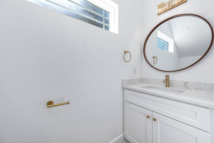 Stylish half bath featuring a quartz vanity, ash blue cabinetry, and elegant gold fixtures.