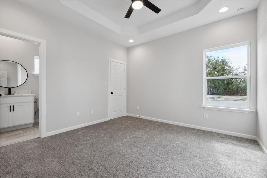 Unfurnished bedroom featuring light carpet, baseboards, recessed lighting, ensuite bath, and a raised ceiling Unfurnished bedroom featuring light carpet, baseboards, recessed lighting, ensuite bath, and a raised ceiling