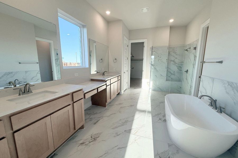Bathroom featuring a freestanding bath, light marble finish flooring, a marble finish shower, double vanity, and a spacious closet