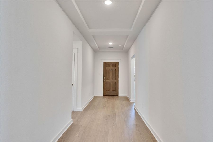 Inviting entryway featuring a warm wood-panel door, light wood-finish flooring, recessed lighting, and a tray ceiling