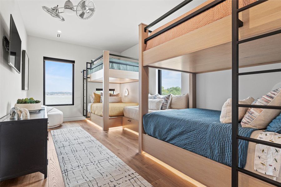 Room featuring two built-in bunk beds with integrated lighting, wood-finish flooring, a wall-mounted television, and an expansive window