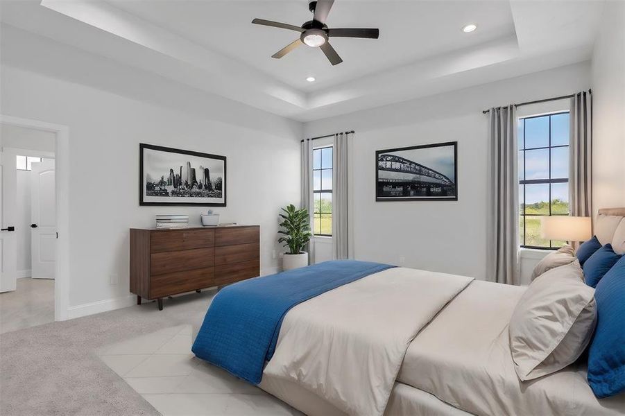 Bedroom featuring light colored carpet, multiple windows, ceiling fan, and a tray ceiling