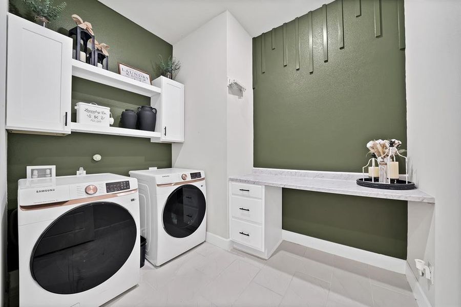 Laundry area featuring built-in cabinetry, an open shelving unit, and a built-in desk with a light-toned countertop Laundry area featuring built-in cabinetry, an open shelving unit, and a built-in desk with a light-toned countertop