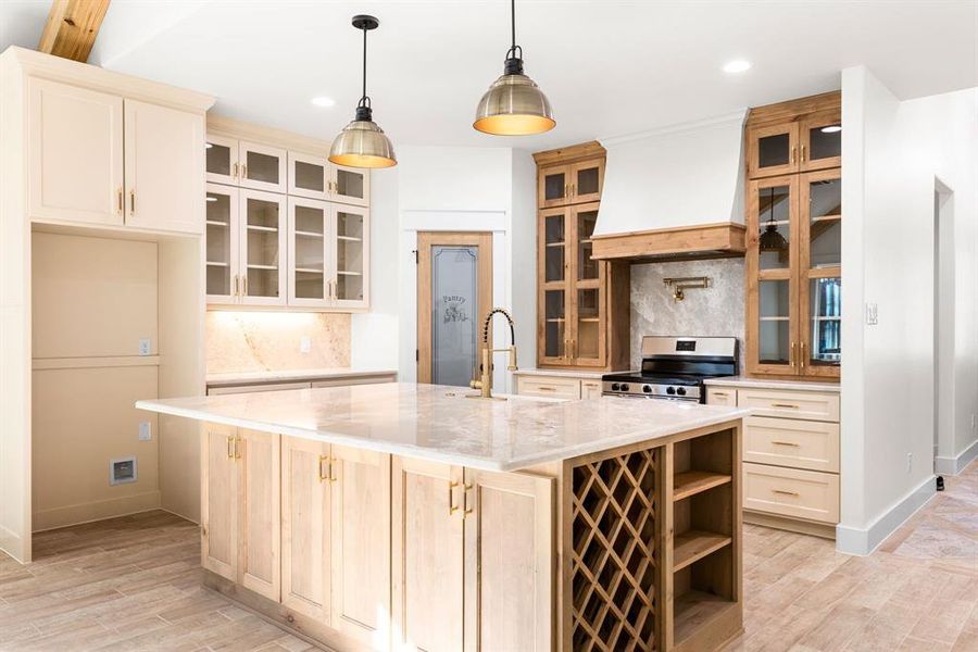 Kitchen featuring backsplash, stainless steel gas range oven, a center island with sink, and custom range hood