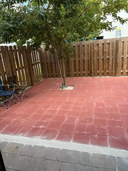 Private outdoor patio featuring square red paver stones, a dedicated tree cutout, and full-height wood privacy fencing