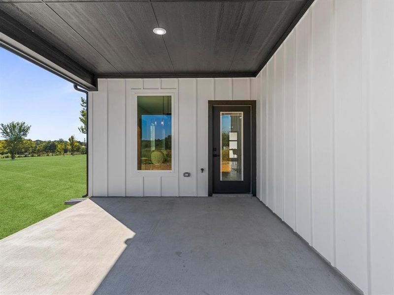 View of exterior entry with board and batten siding, a patio, and a yard