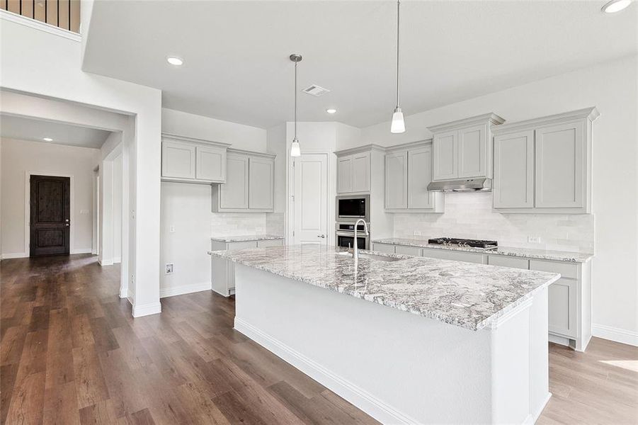 Kitchen featuring stainless steel appliances, wood-type flooring, backsplash, and an island with sink