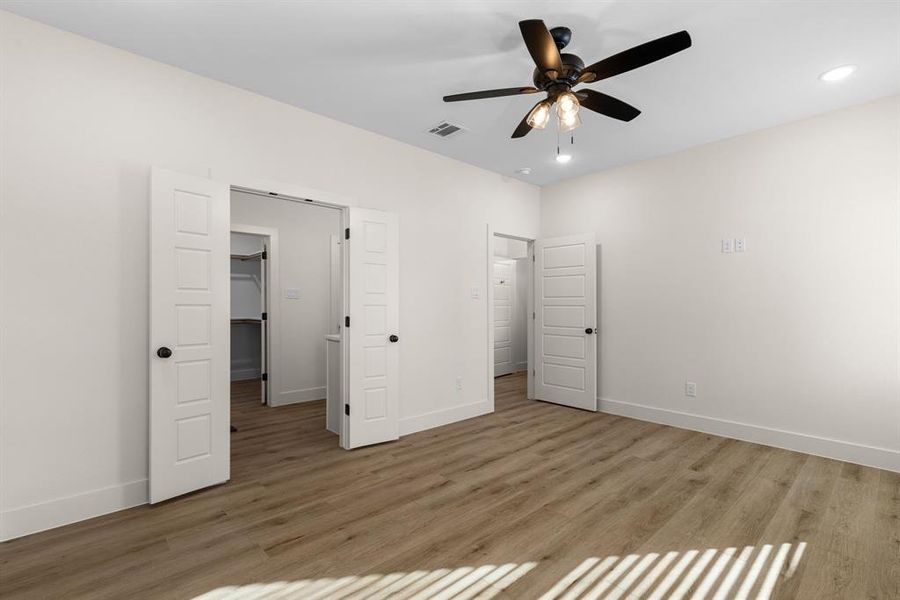 Unfurnished bedroom featuring a spacious closet, hardwood / wood-style floors, and ceiling fan