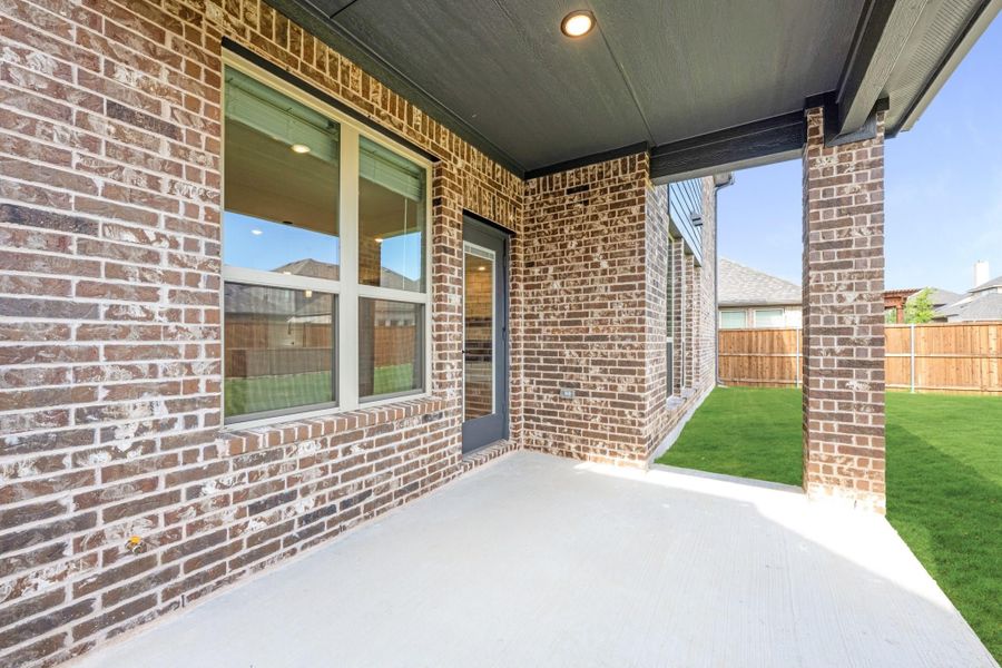 Covered back patio with brick exterior, concrete floor, and fenced grassy backyard
