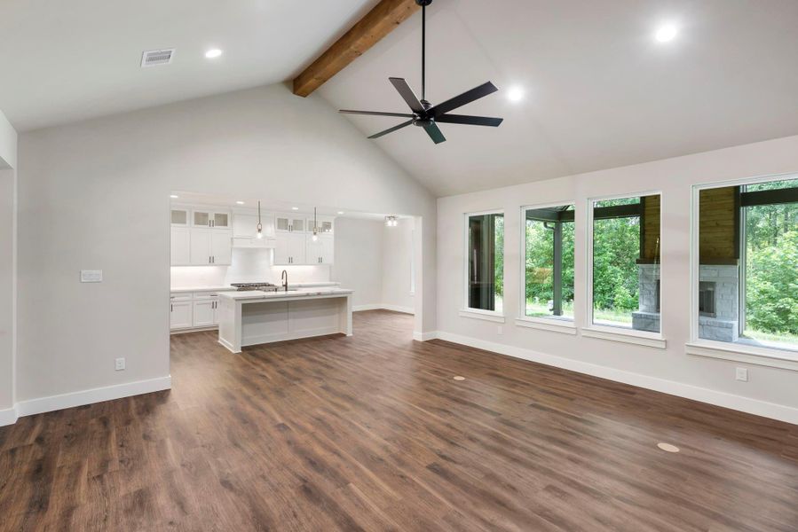 Another view of this spacious open-concept living area features high ceilings, large windows with forest views, and stylish wood flooring. The modern kitchen includes dark cabinetry, an island, and pendant lighting, creating an ideal setting for entertaining.
