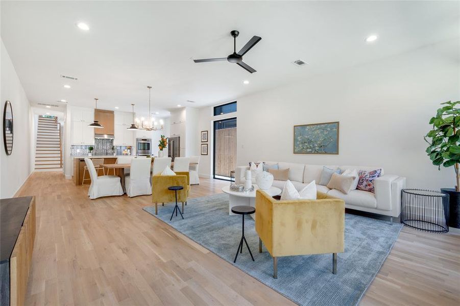 Living room featuring ceiling fan with notable chandelier and light wood-type flooring