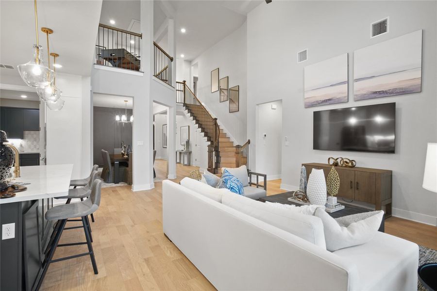 Living room featuring a towering ceiling, light wood finished floors, stairway, and recessed lighting