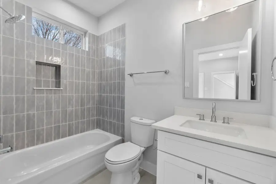 Bright full bath featuring a clean vanity with quartz countertops, modern fixtures, and a tiled tub/shower combination with built-in niche.