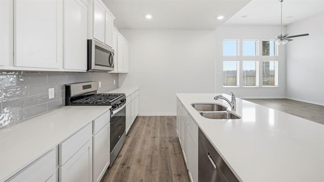 Modern kitchen featuring white cabinetry, light-toned countertops, a stainless steel gas range, and a gray subway tile backsplash