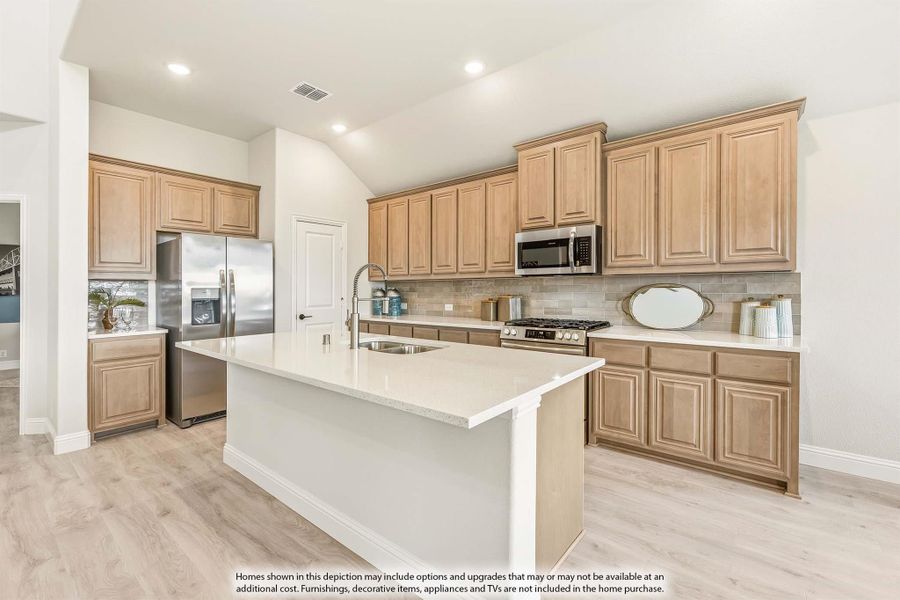 Kitchen with light wood cabinets, center island with sink, stainless steel appliances, and light hardwood floors