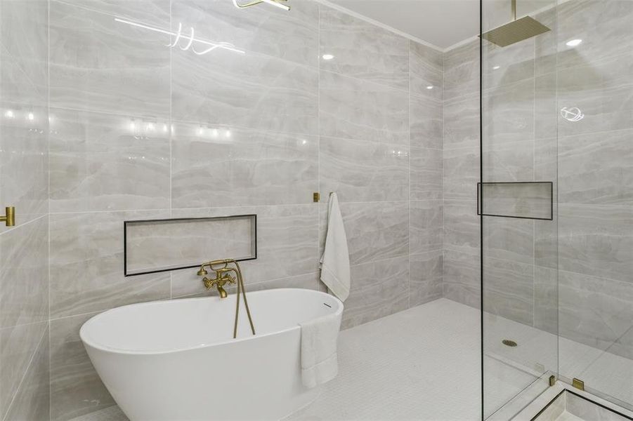 Contemporary bathroom featuring a freestanding soaking tub with brass fixtures, a walk-in shower with a glass enclosure and rainfall showerhead, and light-toned tile walls