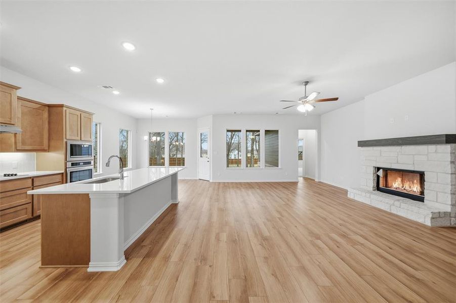 Kitchen with light wood-style floors, a fireplace, a ceiling fan, open floor plan, and a kitchen island with sink Kitchen with light wood-style floors, a fireplace, a ceiling fan, open floor plan, and a kitchen island with sink
