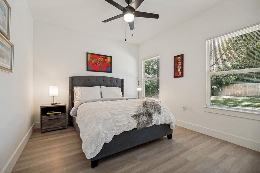 Bright bedroom featuring two windows, wood-finish flooring, and an overhead ceiling fan Bright bedroom featuring two windows, wood-finish flooring, and an overhead ceiling fan