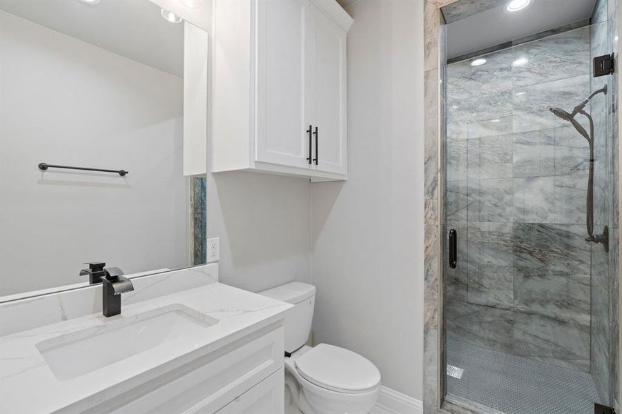 Bathroom featuring a shower with door, vanity, and toilet