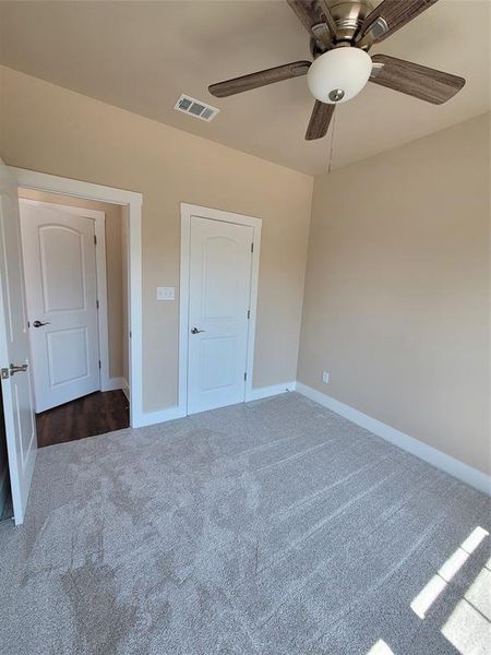 Unfurnished bedroom with dark colored carpet and ceiling fan