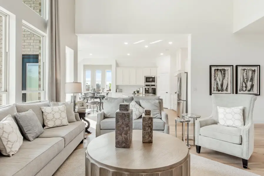 Open-concept living room with gray sofas, high ceilings, and kitchen visible in background