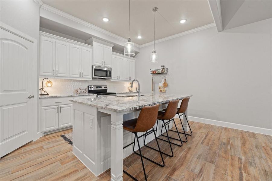 Kitchen featuring light stone countertops, hanging light fixtures, white cabinetry, appliances with stainless steel finishes, and a breakfast bar
