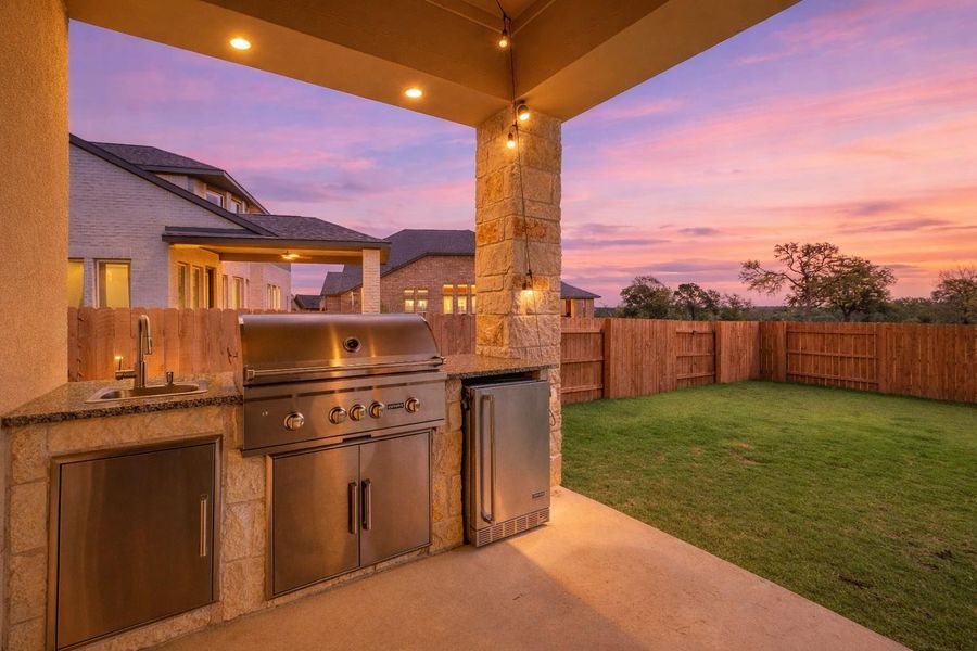 The property features an outdoor kitchen with a built-in stainless steel grill, a sink, and a refrigerator, all set within a stone and granite countertop