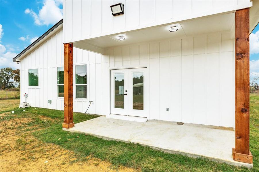 Rear view of house with board and batten siding, a patio area, french doors, and a lawn Rear view of house with board and batten siding, a patio area, french doors, and a lawn