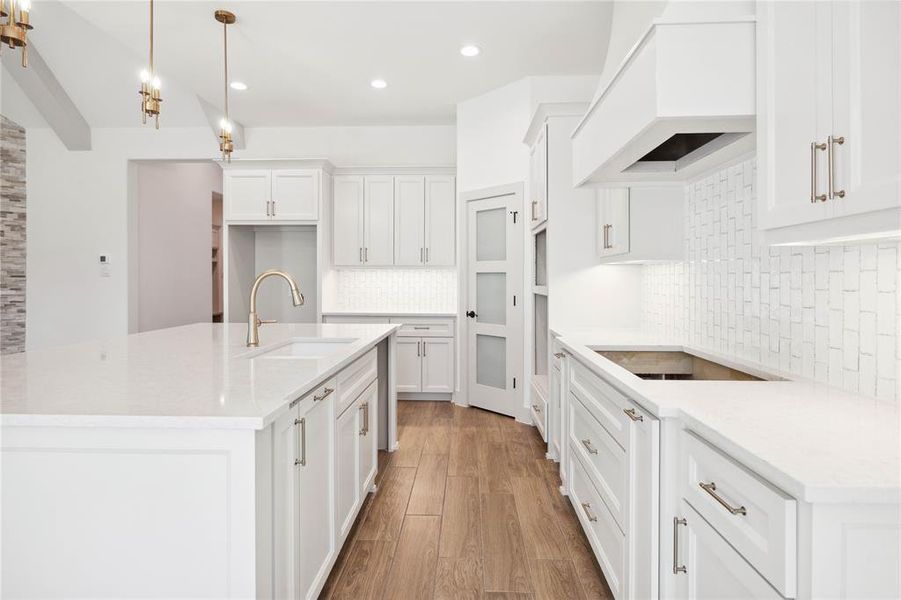 Kitchen with hanging light fixtures, light stone counters, premium range hood, stovetop, and white cabinets