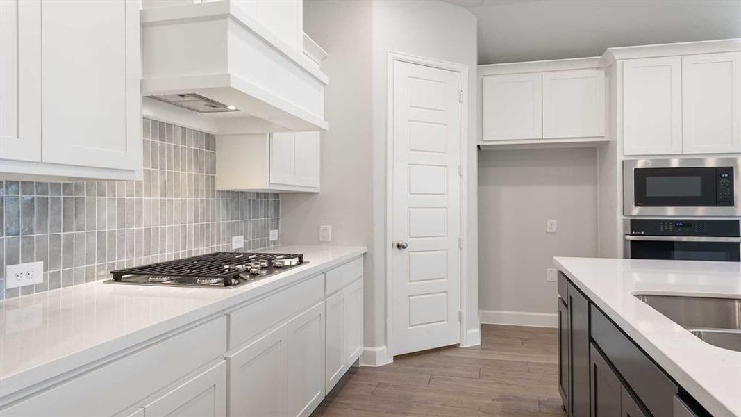 Kitchen with white cabinetry, tasteful backsplash, light hardwood / wood-style floors, custom exhaust hood, and appliances with stainless steel finishes