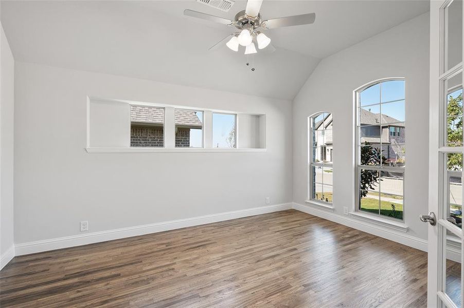 Empty room featuring wood finished floors, plenty of natural light, lofted ceiling, and a ceiling fan