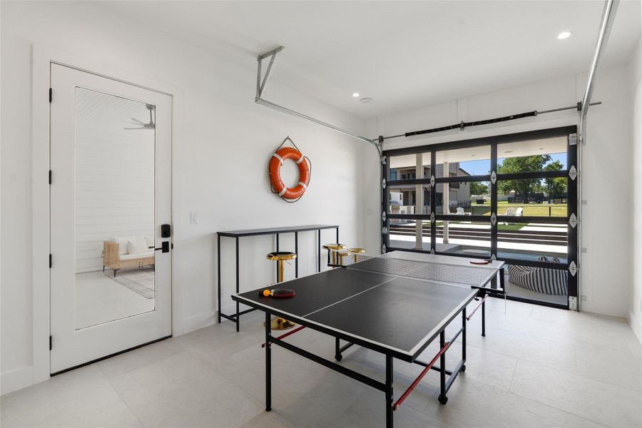 A well-lit recreational room offers a ping-pong table and access to the outdoors through a glass garage door. A well-lit recreational room offers a ping-pong table and access to the outdoors through a glass garage door.
