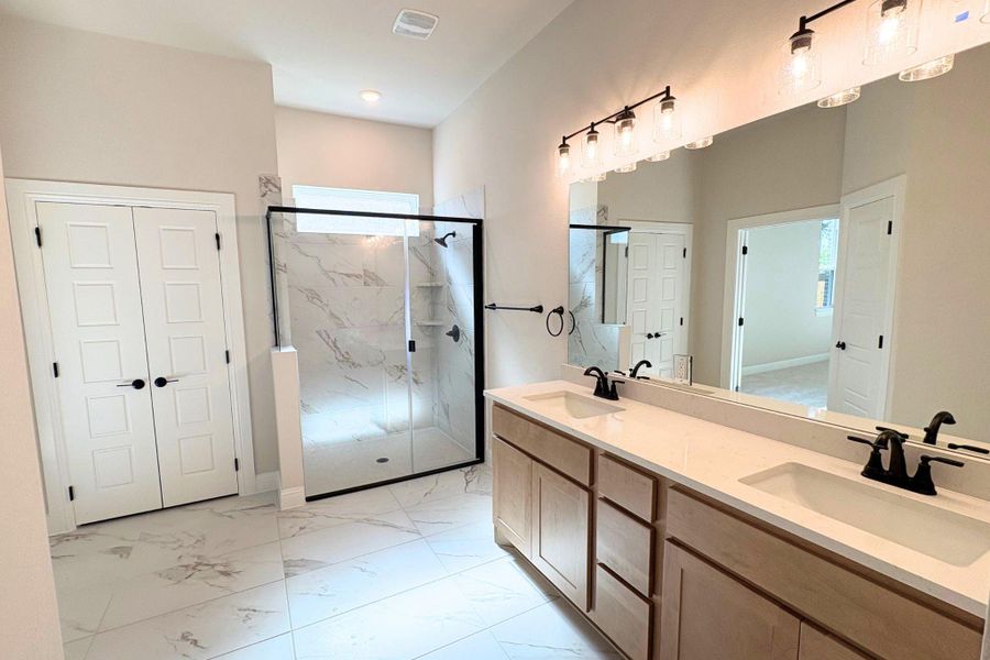 Polished tile flooring and a dual-sink vanity anchor this contemporary primary bath oasis. Polished tile flooring and a dual-sink vanity anchor this contemporary primary bath oasis.