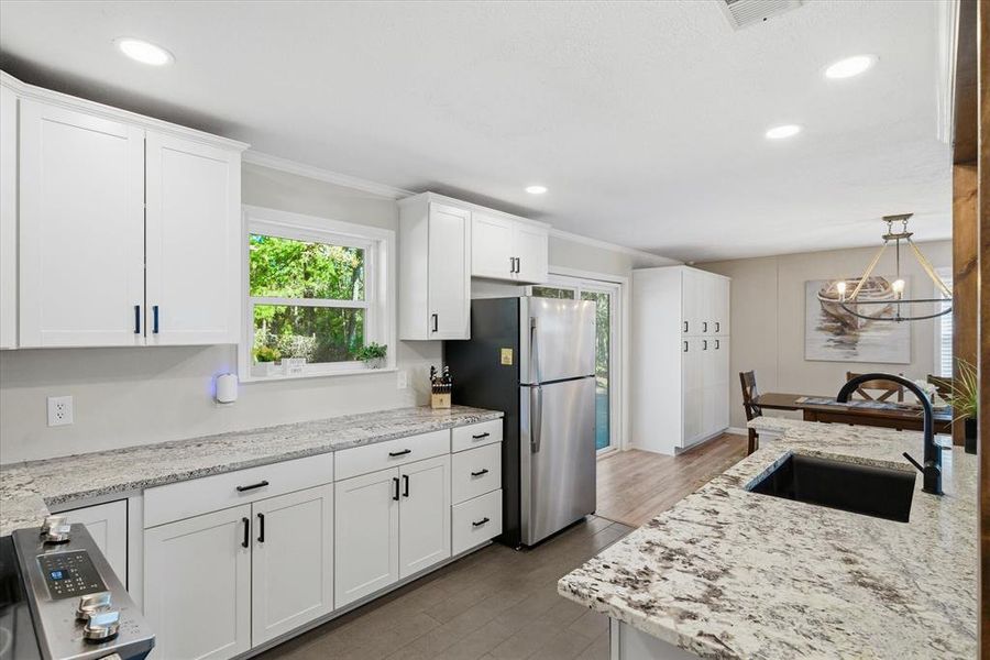 Modern kitchen featuring white shaker cabinetry with matte black hardware, speckled countertops, a large undermount sink with a gooseneck faucet, recessed lighting, and wood-finish flooring