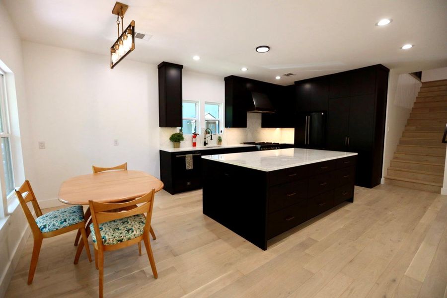 Kitchen with dark cabinetry, a kitchen island, high end black fridge, light stone countertops, and light wood-type flooring