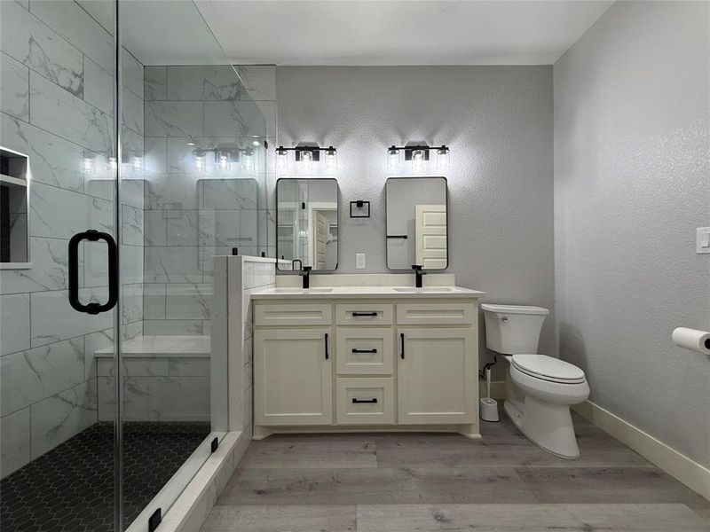 Full bathroom with double vanity, a textured wall, light wood finished floors, and a marble finish shower