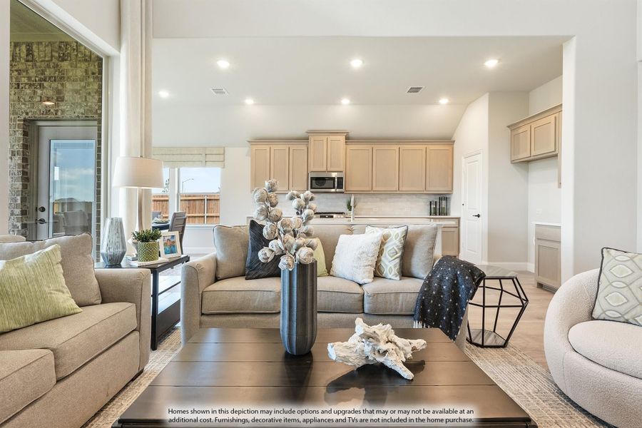 Open-concept living room with neutral sofas and coffee table, open to kitchen with tan cabinets and recessed lighting