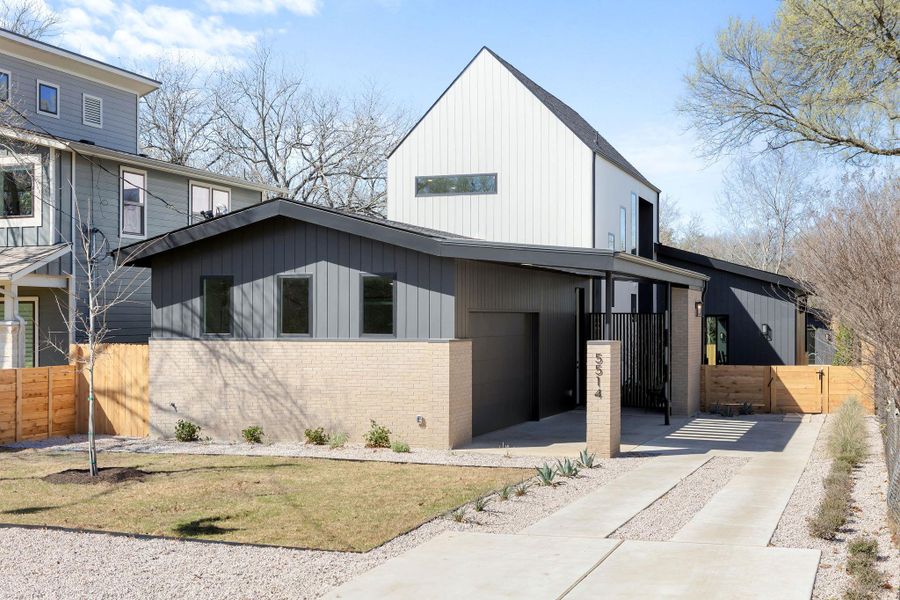 View of front of property featuring fence, brick siding, driveway, and a gate