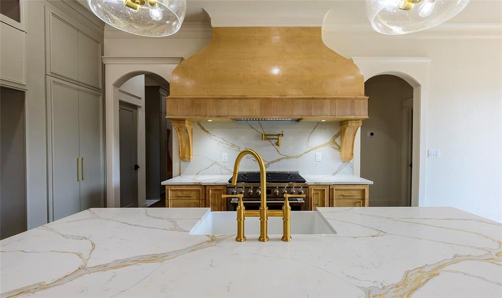 Kitchen featuring light stone countertops, high end stainless steel range, tasteful backsplash, wood finish cabinets, and arched walkways