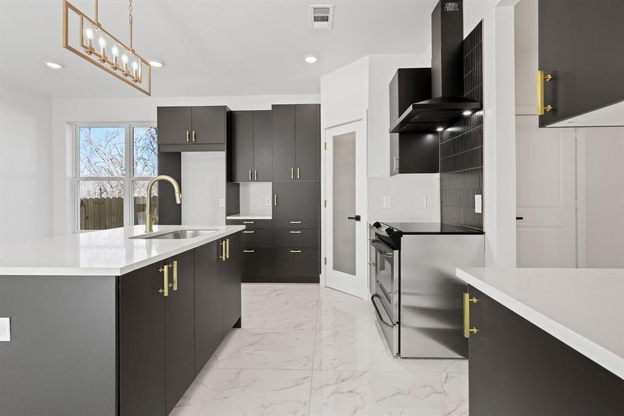 Kitchen with electric stove, sink, pendant lighting, wall chimney range hood, and a kitchen island with sink